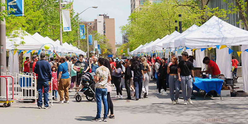 tents and trees lining street with crowd of people engaged in activities covered by tents