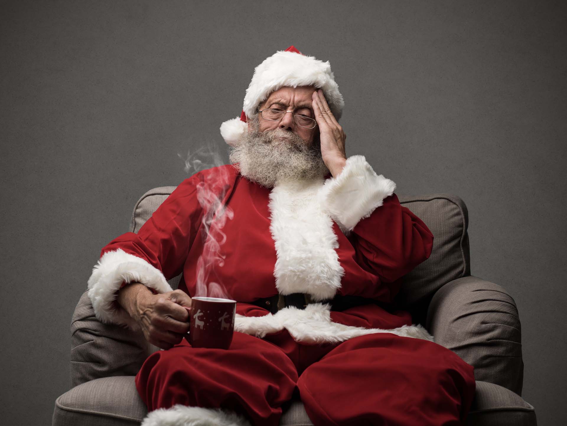 Santa sitting holding his head and drinking coffee