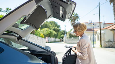 Mature woman taking laptop bag from a car boot on the street.