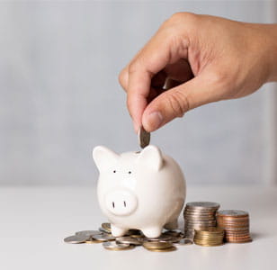 A hand dropping a coin into a piggy bank