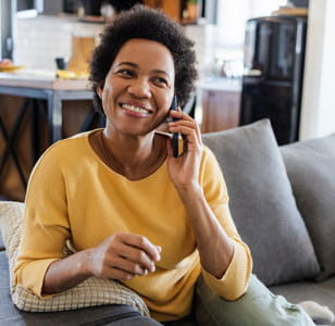 Person in a yellow top sitting on a sofa and speaking on a phone