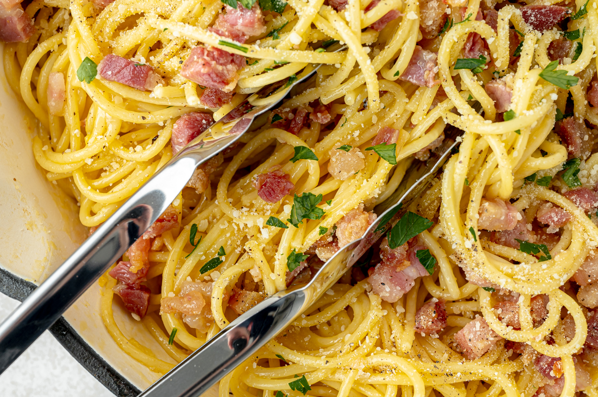 overhead shot of tongs tossing carbonara