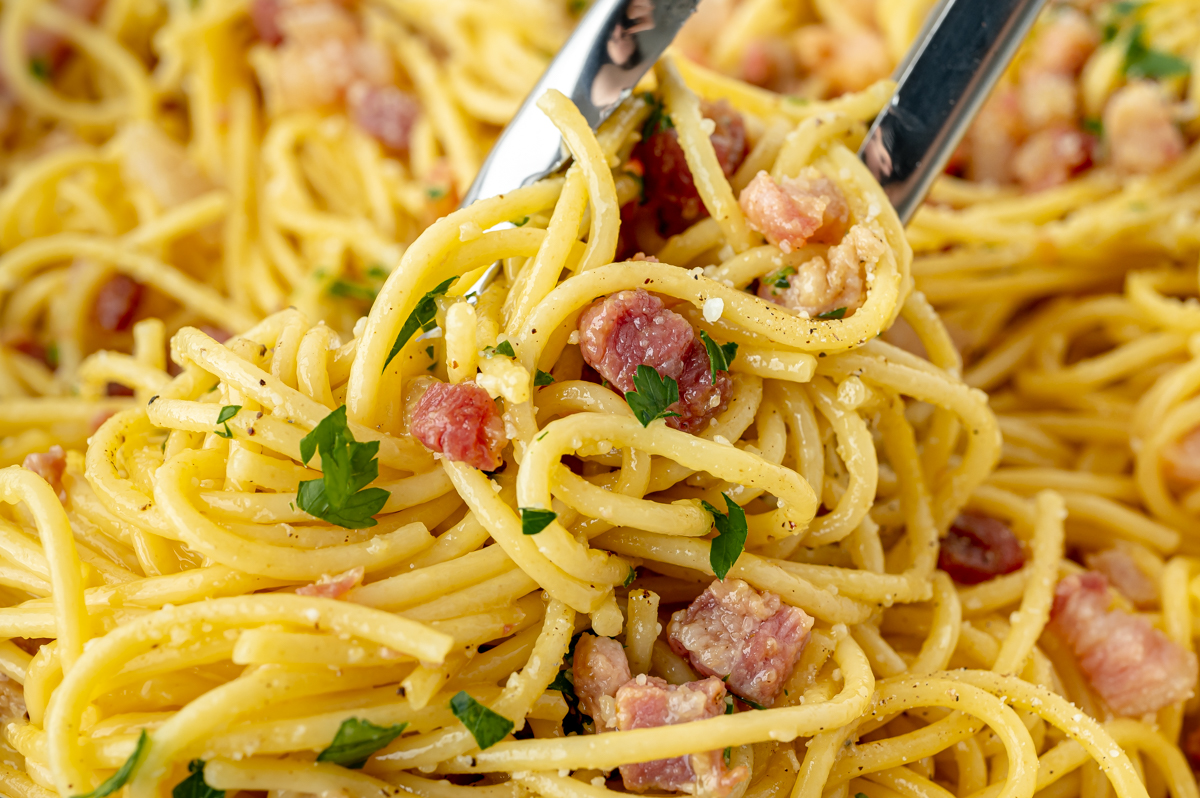 angled shot of tongs tossing carbonara