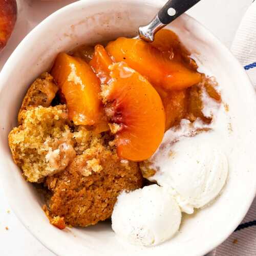 overhead close up view of peach cobbler in white bowl