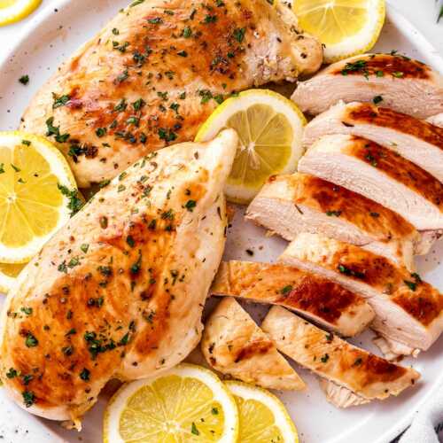 overhead view of marinated grilled chicken on white plate with lemon slices