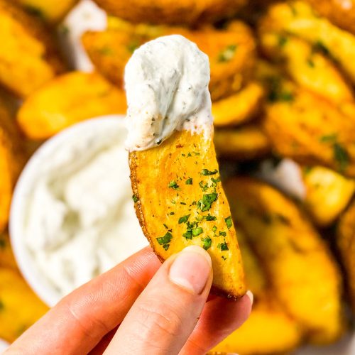 female hand holding a potato wedge covered with sour cream