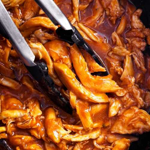 overhead close up view of bbq pulled chicken in crock with tongs