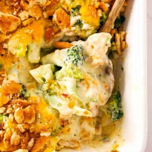 frontal close up view of wooden spoon scooping up broccoli cheese casserole from a white baking dish