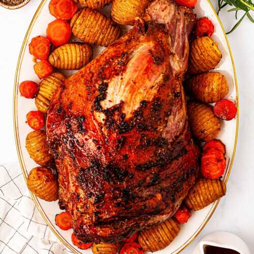 overhead view of roasted leg of lamb on platter with potatoes and carrots