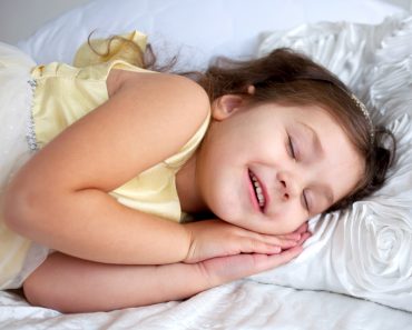 Happy smiling kid sleeping and smiling in her sleep. Dream the little princess on a white bed close-up speaking in dream.