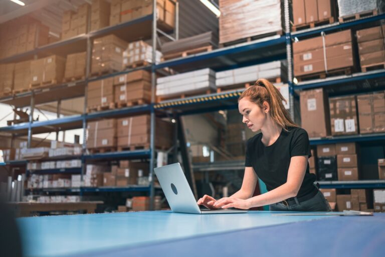 woman uses laptop in the middle of an ecommerce warehouse