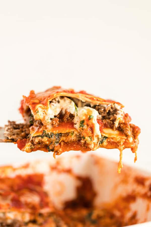 Spatula lifting a slice of cheesy, saucy lasagna out of baking dish.