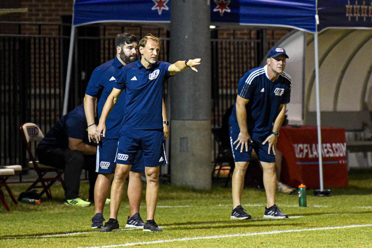 The University of Illinois-Chicago associate head coaches for men's soccer, Minos Vlamakis (back) and Aleksey Korol (front) stand on the sidelines with head coach Sean Phillips (right)