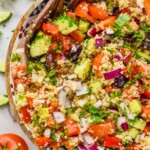 overhead view of a bowl of greek quinoa salad garnished with parsley, with cucumbers and tomatoes off to the side of the bowl