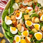 overhead view of spinach bacon salad with hard boiled eggs, croutons, water chestnuts in a white bowl