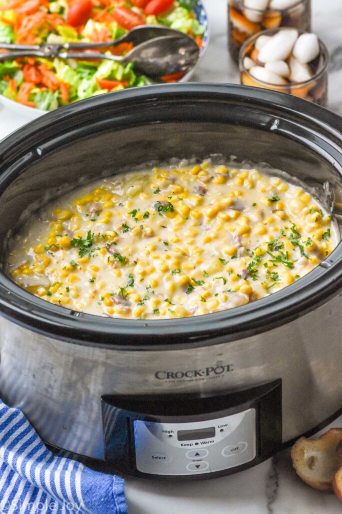 Crockpot of Crockpot Corn Chowder with salad and drinks beside.