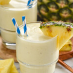 Two glasses of Pineapple Smoothie with straws and fresh pineapple wedge on the rim