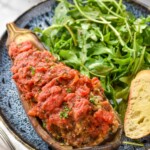 Plate of Stuffed Eggplant topped with fresh parsley with arugula salad and piece of bread beside