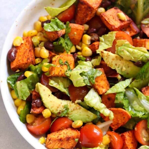 A bowl of salad with lettuce, cherry tomatoes, avocado slices, roasted sweet potato chunks, corn, and black beans.