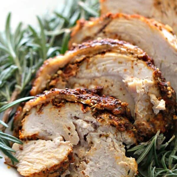 Sliced Instant Pot Turkey Breast garnished with fresh rosemary on a white plate.