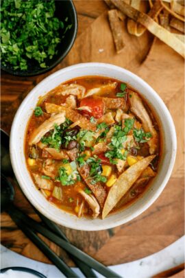 Top view of a bowl of Easy Crock Pot Chicken Tortilla Soup topped with fresh cilantro, with a bowl of additional chopped cilantro in the background.