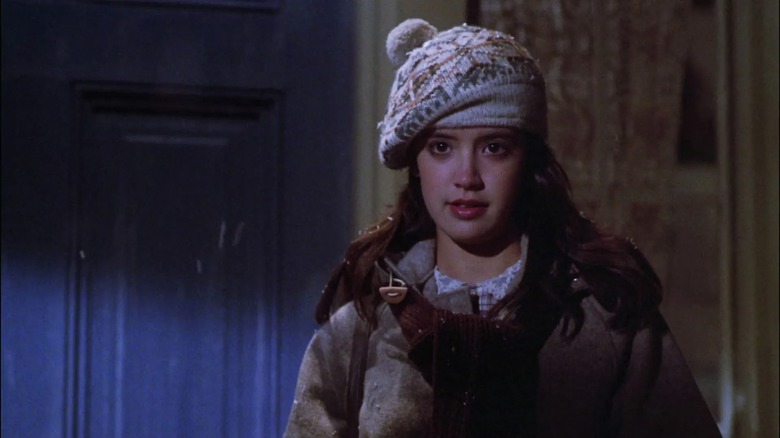 Phoebe Cates in winter wear and a knit cap, standing by a door in Gremlins