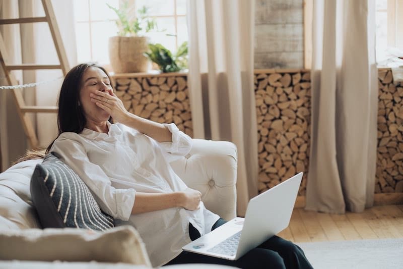 A woman is yawning while trying to work on a laptop