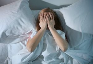 Young woman lying in bed with hands over face