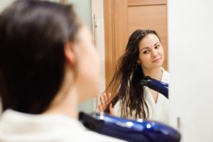 A woman dries her hair with a hair dryer after taking a shower