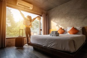 A woman with a suitcase stretches in front of the window of her Airbnb