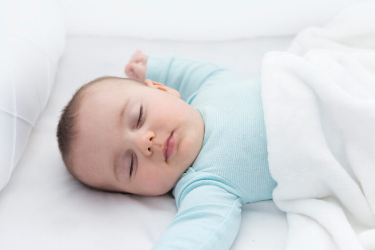 Baby sleeping in bed with their arms open