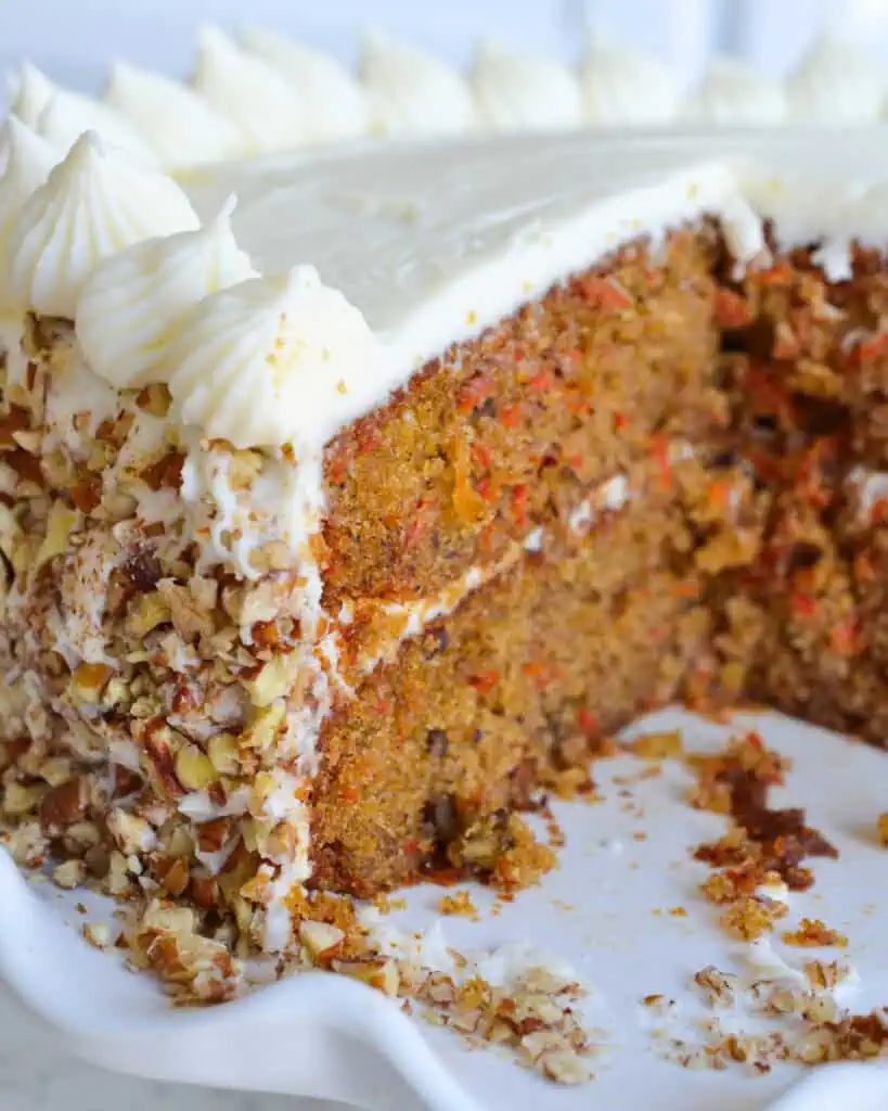 The view of the inside of carrot cake with cream cheese frosting and pecans on a white cake stand. 