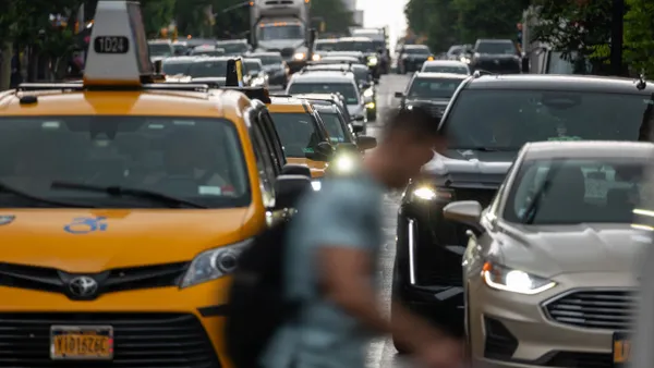 A blurred person crosses in front of an endless line of traffic.