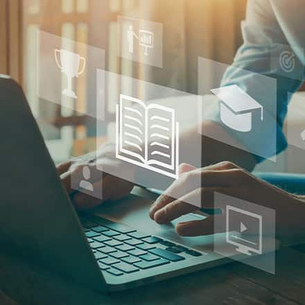 A person using a laptop to research what credit hours are with floating icons of a book, graduation cap, magnifying glass, person and trophy.