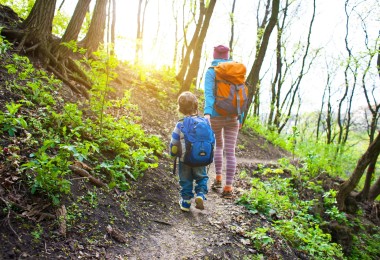 mom and child hiking on trail in forest with sun shining through trees