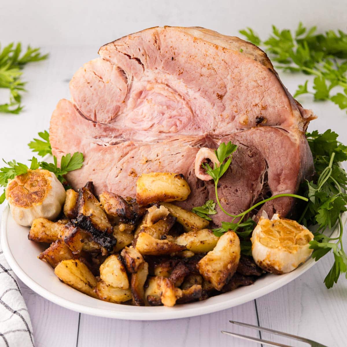 A white serving plate with a half country ham and skillet browned potatoes.