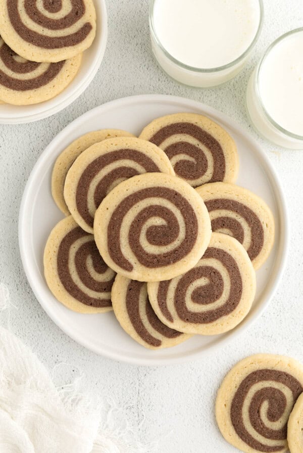 Chocolate and Vanilla Swirl Cookies sitting on a white plate for serving with two glasses of milk on the side.