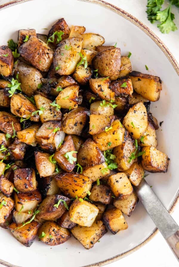 Crispy pan fried potatoes and onions in a large white serving bowl with a spoon for serving.