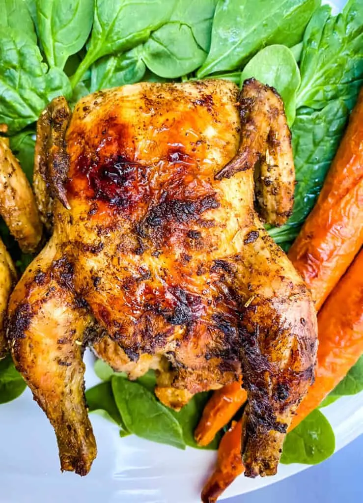 air fryer Cornish hens, fresh spinach, and carrots on a white plate