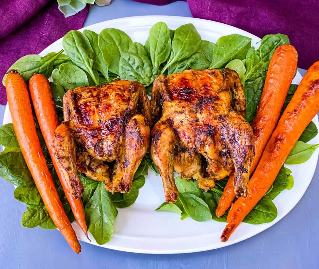 air fryer Cornish hens, fresh spinach, and carrots on a white plate