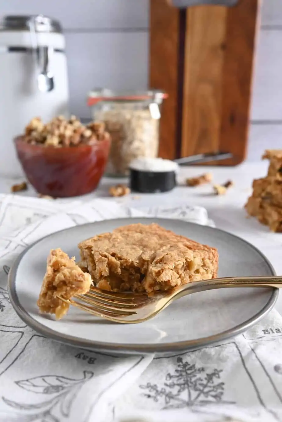 Fork taking a bite from a maple walnut blondie on a gray plate.