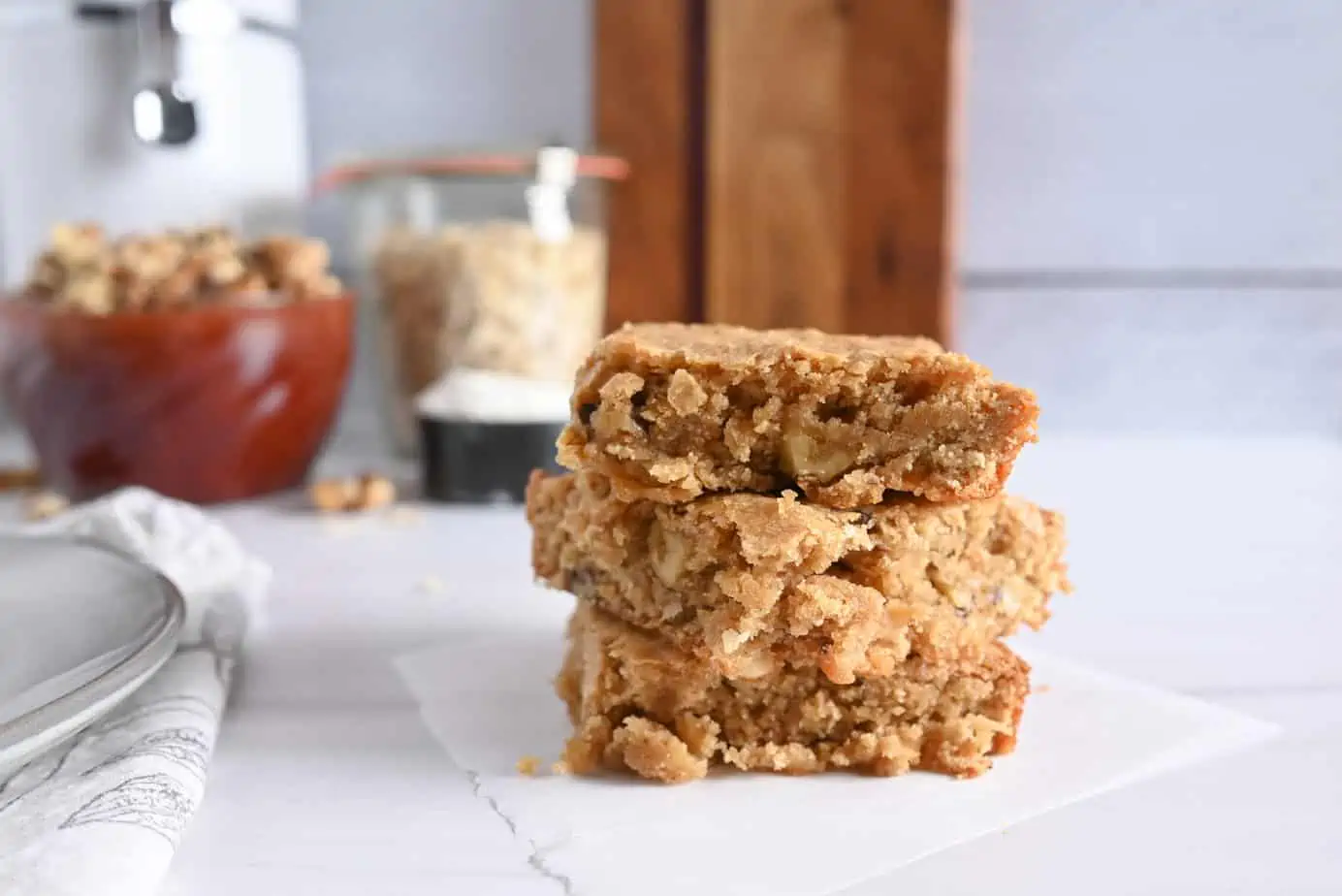 Three maple walnut blondies stacked on a piece of parchment paper on a marble countertop.