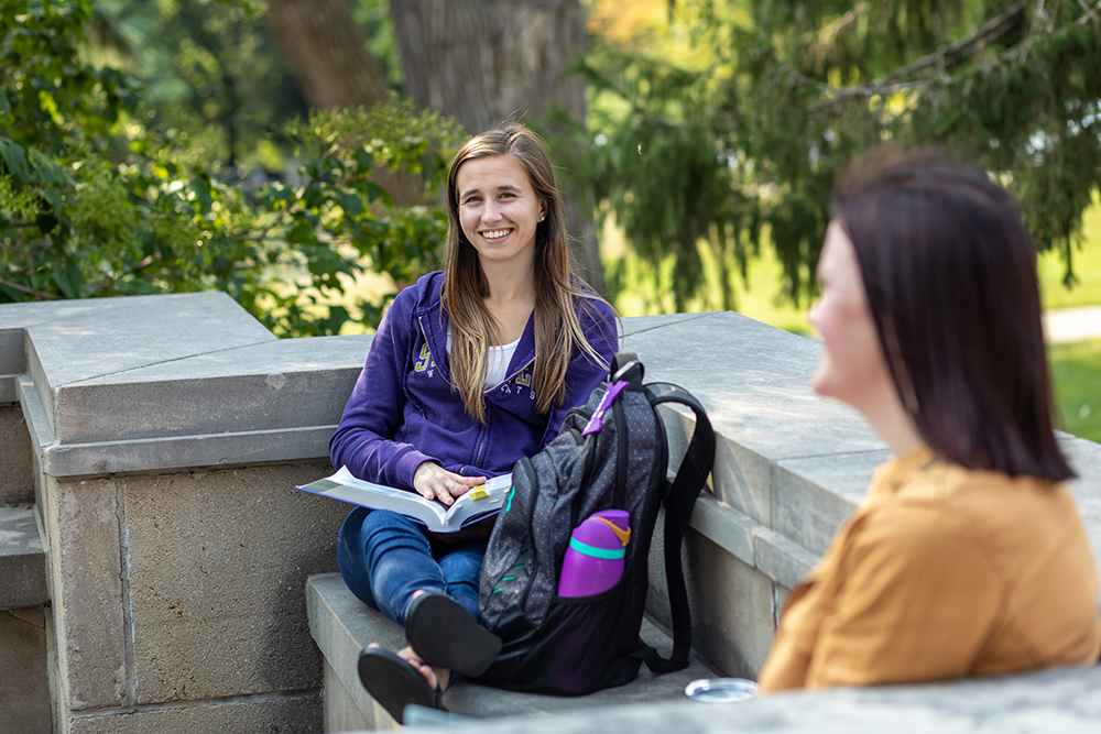 Two laughing students, studying outside on campus.