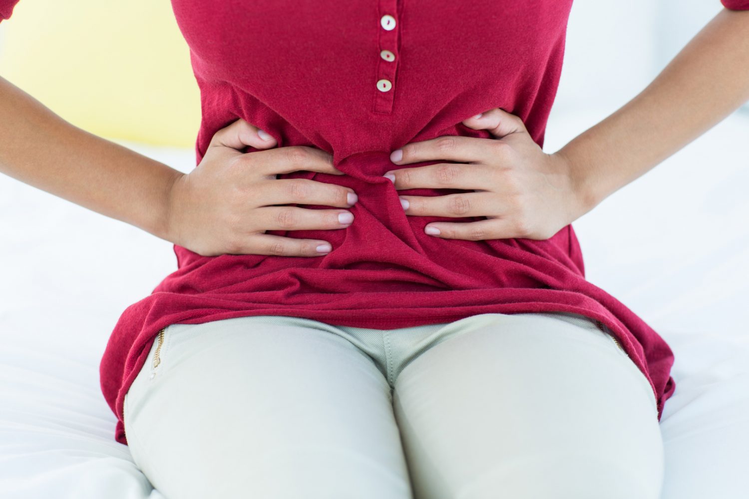 Woman sitting on bed with stomach pain at home