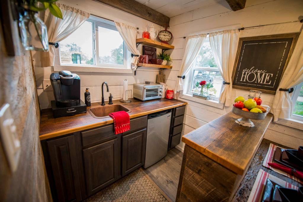 A close up of the kitchen area, with a small metal sink, single fridge and some shelves.