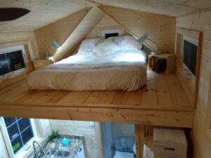 A view mainly of the upstairs bedroom loft area, with side windows. Also shows some of the kitchen area below.