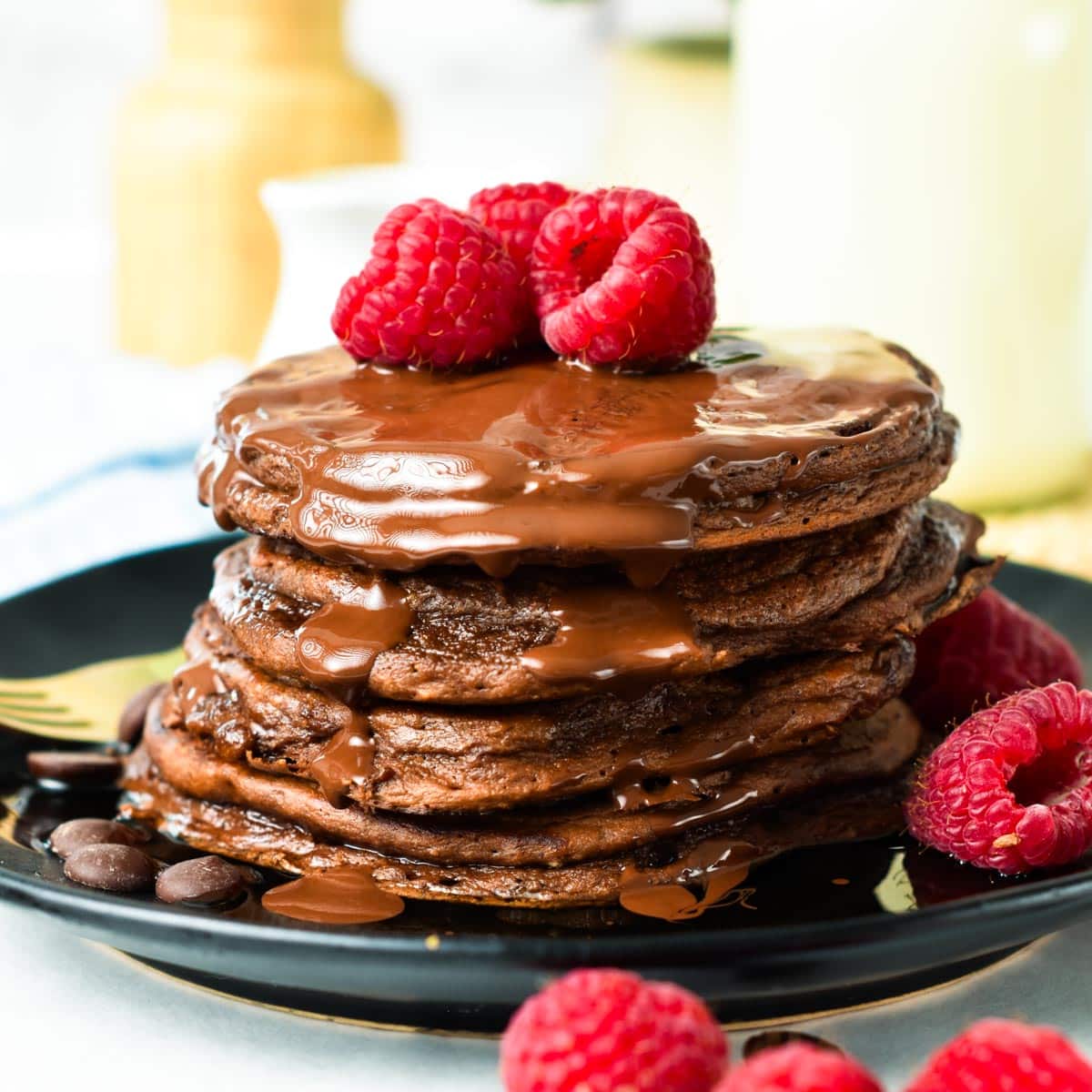 a stack of Chocolate Protein Pancakes with chocolate sauce on top and fresh raspberries