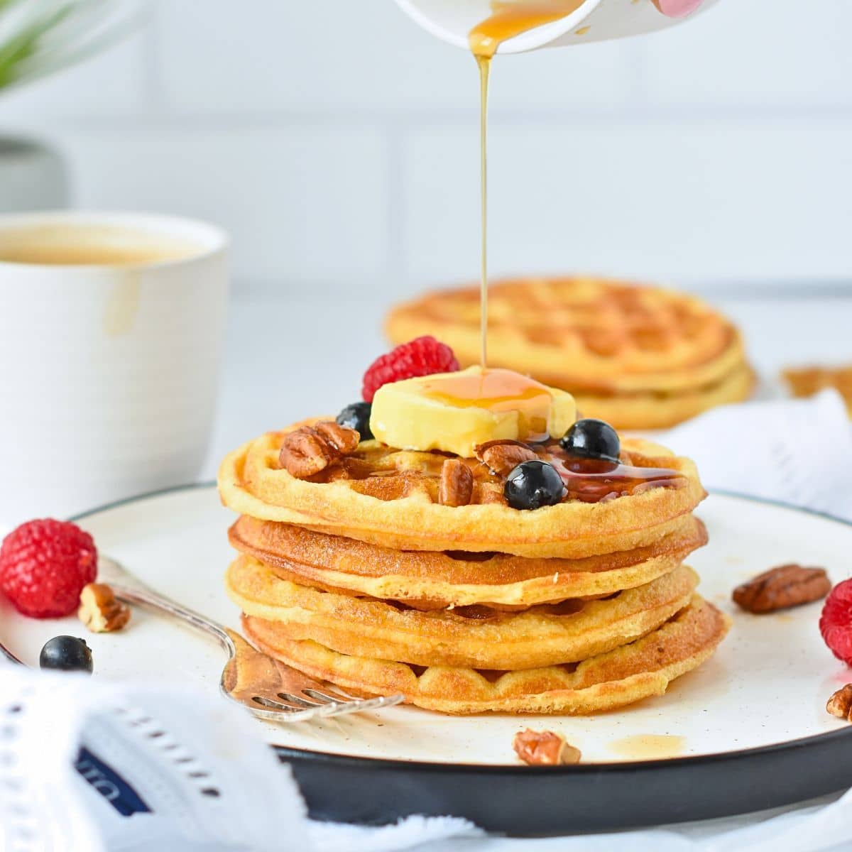 Coconut Flour Waffles stacked on a plate with maple syrup poured on top