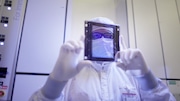 An Intel employee displays a reticle, or photomask, used to create a pattern of circuitry on a silicon wafer. Ultraviolet light shining through the reticle imprints a microscopic pattern on the wafer.