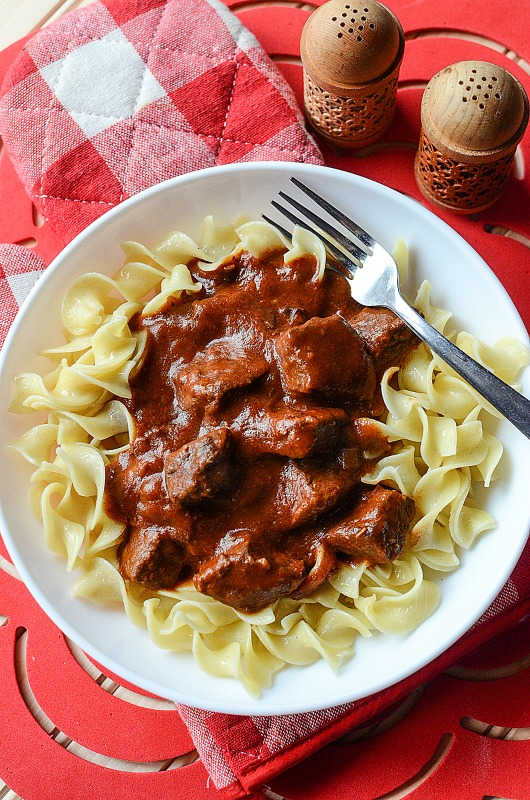 crockpot goulash on a white plate with egg noodles and a fork